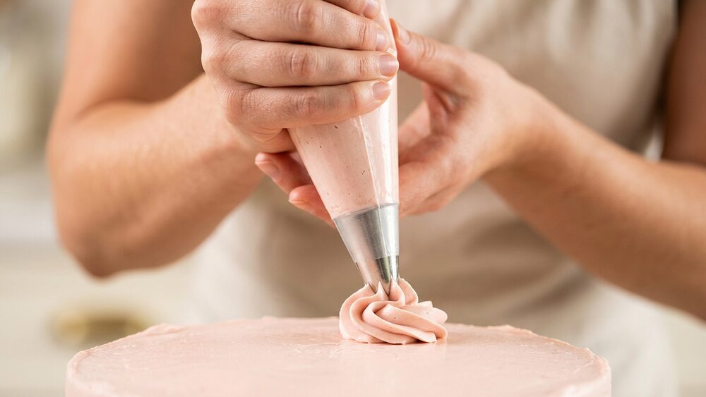Hands piping a buttercream star swirl