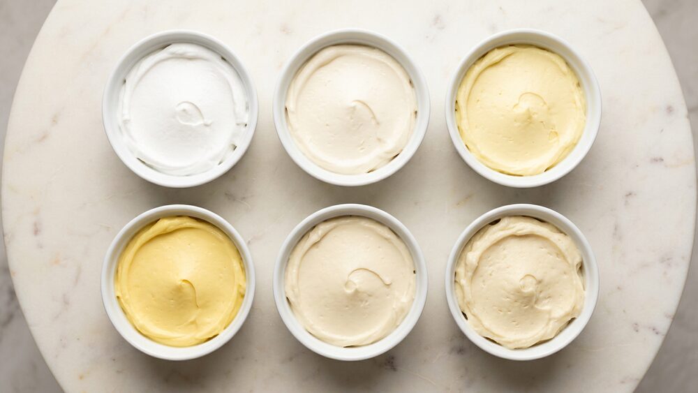 Six bowls of buttercream in different shades